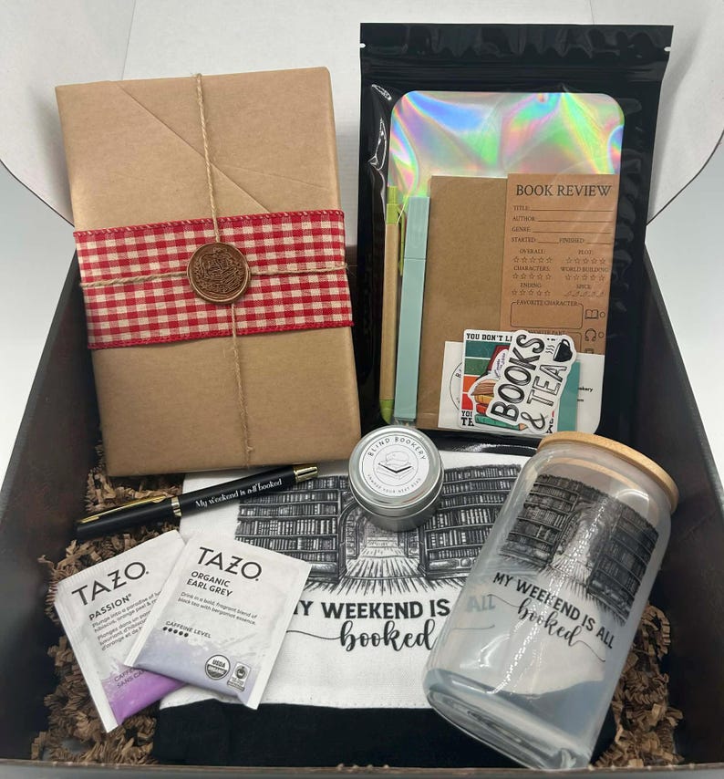 May include: A gift box filled with book-themed items. Includes a wrapped book with a red and white checkered ribbon, a pen, tea bags, a candle, a glass jar, and a tote bag with the text "My weekend is all booked."