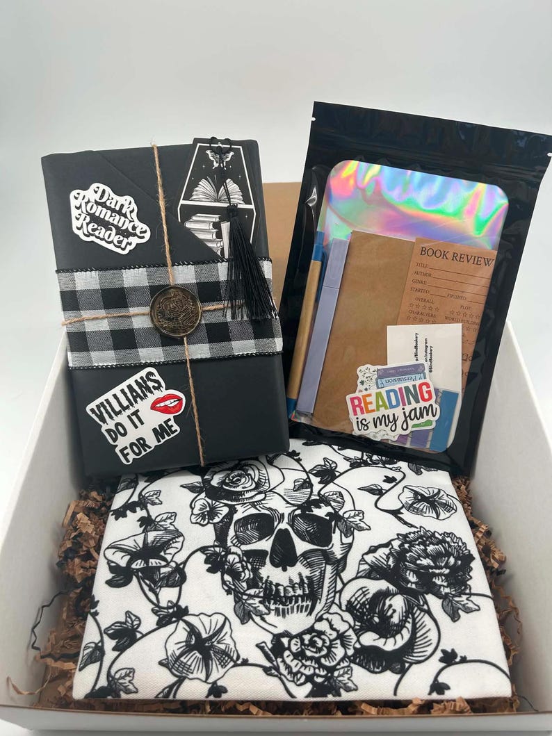 May include: A gift box containing a black-wrapped book with a buffalo plaid ribbon, a wax seal, and stickers reading Dark Romance Reader and VILLAINS DO IT FOR ME. Includes a holographic pouch with stationery and a white cloth featuring a black skull print.