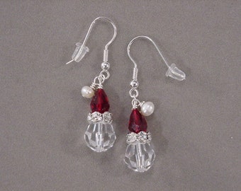 May include: A pair of silver dangle earrings with clear crystal teardrop-shaped beads, red glass beads, and white pearl beads.