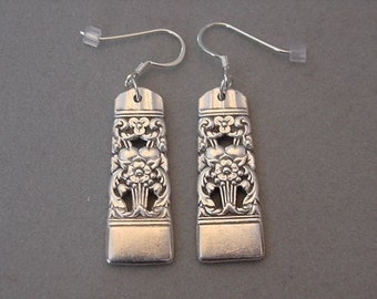 May include: A pair of silver earrings made from repurposed silverware. The earrings feature a floral design with a delicate, intricate pattern.