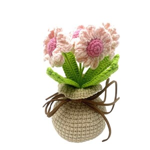 May include: A crocheted bouquet of pink flowers in a beige crocheted pot with a brown ribbon.