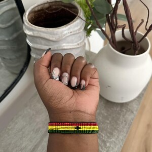 Op de afbeelding: Een kralenarmband met de kleuren van de Ghanese vlag: rood, geel, groen en een zwarte ster in het midden.