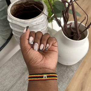 May include: A beaded bracelet with black, red, yellow, and white beads. The bracelet is on a person's wrist.