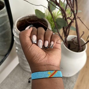 Könnte beinhalten: Ein blaues Armband aus Perlen mit einem gelben und roten Chevron-Muster. Das Armband befindet sich am Handgelenk.