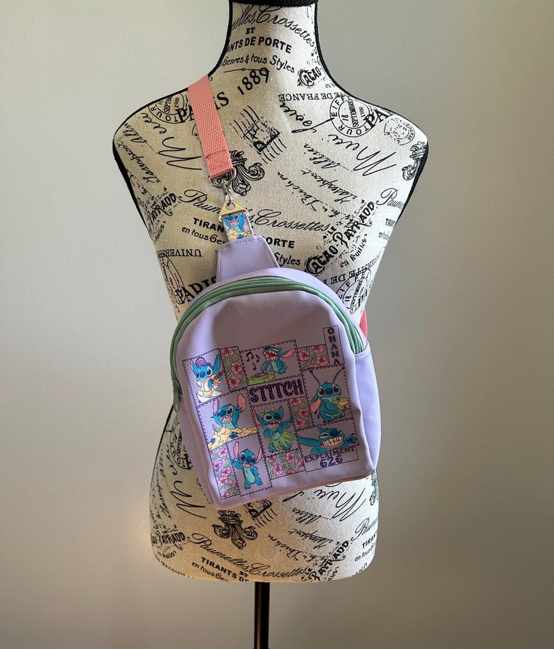 May include: A purple and green Stitch backpack with a pink adjustable strap. The backpack features a patchwork design with images of Stitch in various poses. The text "Stitch" and "Ohana" are printed on the backpack.