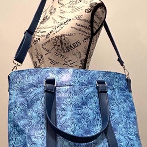 May include: Blue tote bag with a floral pattern and dark blue handles and shoulder strap. The bag is displayed on a mannequin with text that says "Paris 1889".