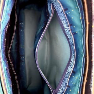 May include: Interior view of a tote bag with multiple compartments. The bag features a blue and teal patterned fabric with a zipper closure. The interior lining is a solid light blue color. The bag has a celestial theme with stars.