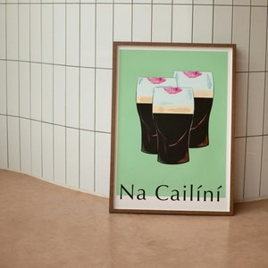 May include: A framed print with a green background featuring three glasses of dark beer with pink lips on the rim. The text "Na Cailíní" is printed at the bottom of the print.