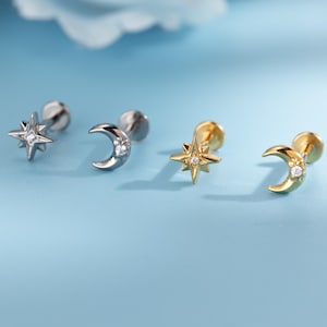 May include: Four stud earrings with celestial designs. Two are silver-toned, featuring a star and a crescent moon, each with a small, clear gem. The other two are gold-toned, with a star and a crescent moon, each with a small, clear gem.