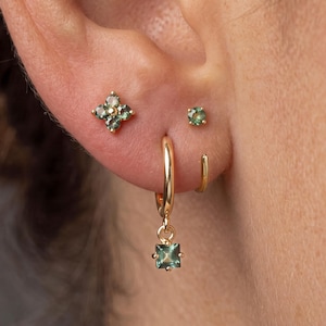 Può includere: Un set di orecchini in oro composto da un perno a forma di fiore con quattro pietre verdi, un piccolo perno con singola pietra verde, un cerchio in oro semplice e un cerchio in oro con un ciondolo a pietra verde di taglio quadrato.