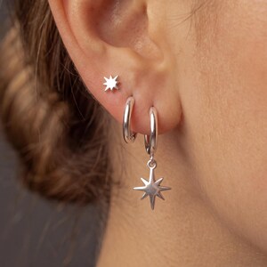 Peut inclure: Un ensemble de trois boucles d'oreilles argentées comprenant un petit clou en forme d'étoile, un anneau simple et un anneau orné d'une breloque étoile à huit branches. Les bijoux sont polis et présentent une finition métallique.