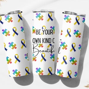 May include: White tumbler with a repeating pattern of colorful puzzle pieces and ribbons. One tumbler features the text "BE YOUR OWN KIND OF Beautiful". The design includes rainbow, yellow, and blue elements. The tumblers have a silver lid.