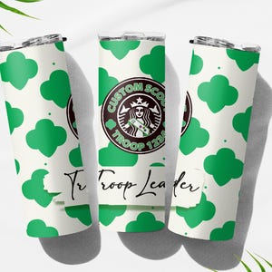 Könnte beinhalten: Drei weiße isolierte Becher mit einem grünen Kleeblattmuster. Einer hat ein individuelles Logo mit einem Pfadfinderinnen-Design und dem Text "CUSTOM SCOUTS TROOP 123". Der Text "Jr Troop Leader" ist ebenfalls sichtbar.