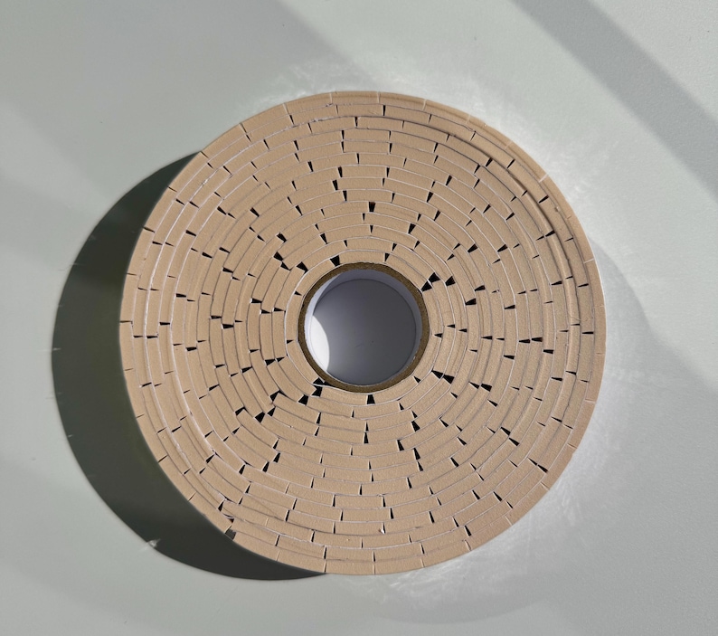 May include: A roll of brown tape with a serrated edge. The tape is wound around a white core.