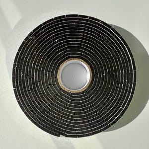 May include: A roll of black foam weather stripping tape. The tape is wound tightly and has a white core.