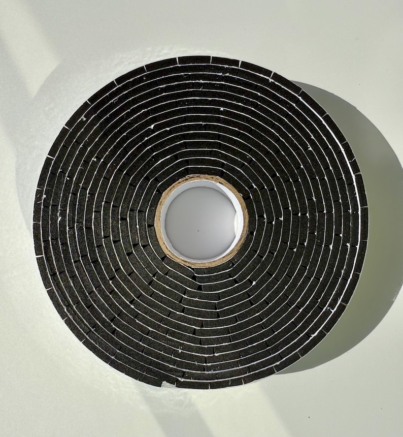 May include: A roll of black foam weather stripping tape. The tape is wound tightly and has a white core.