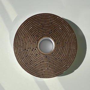 May include: A roll of brown weather stripping tape with a serrated edge. The tape is rolled up in a circle with a hole in the centre.