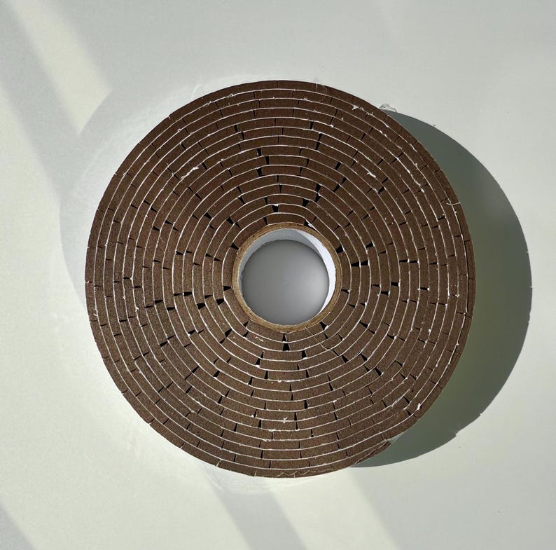 May include: A roll of brown weather stripping tape with a serrated edge. The tape is rolled up in a circle with a hole in the centre.