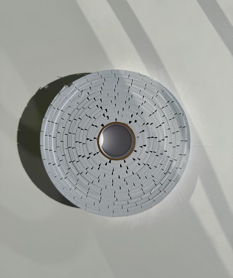 May include: A roll of white adhesive tape with a serrated edge. The tape is wound around a cardboard core.