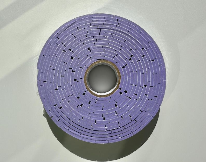 May include: A roll of purple tape wound into a circle. The tape is made of many small squares.