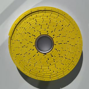 May include: A yellow roll of tape with a circular shape. The tape is made up of small, rectangular pieces that are stacked on top of each other.