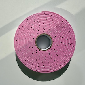 May include: A roll of pink foam tape with a white core. The tape is wound in a spiral pattern.