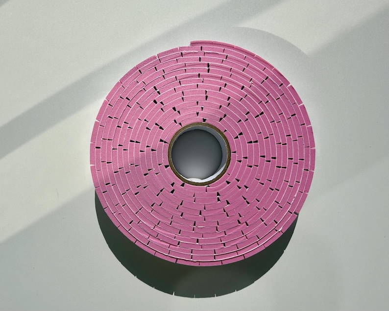 May include: A roll of pink foam tape with a white core. The tape is wound in a spiral pattern.