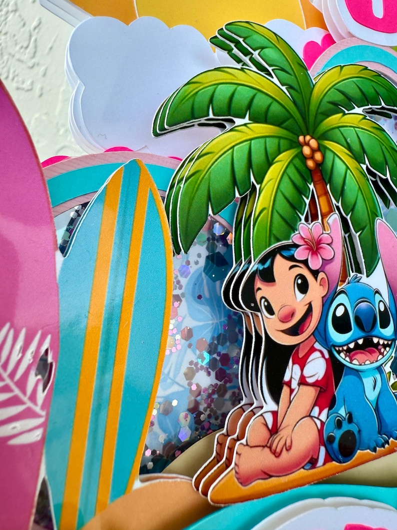 May include: A layered papercraft with a tropical theme. It features a palm tree, surfboards, and cartoon characters Lilo and Stitch. The colour scheme is vibrant, with shades of pink, blue, green, and yellow.