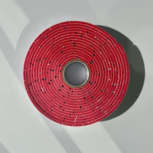 May include: A red circular roll of tape with a hole in the centre. The tape is made of many layers of red material.