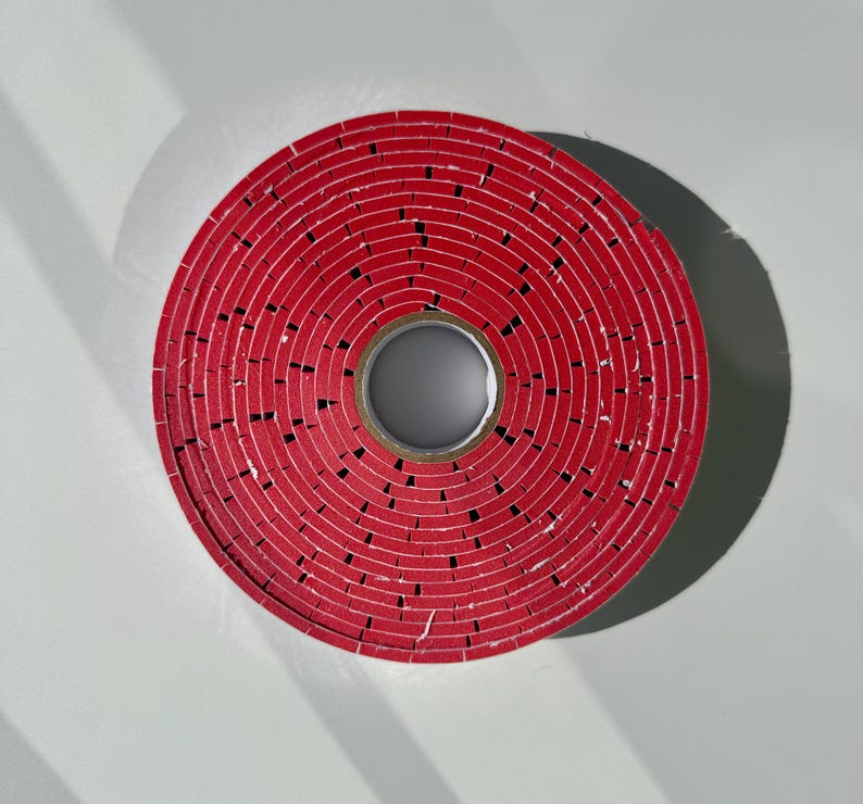 May include: A red circular roll of tape with a hole in the centre. The tape is made of many layers of red material.
