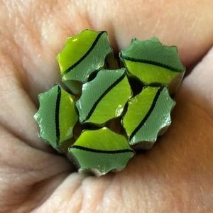 May include: A cluster of six small, star-shaped polymer clay canes featuring a vibrant lime green and pale mint green colour palette. Each individual piece displays a distinct, dark, thin, serrated black line running through the centre.
