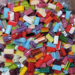 Puede incluir: Primer plano de una variedad de caramelos duros de colores. Los caramelos son cilíndricos y presentan rayas, motivos florales y otros diseños en tonos rojos, amarillos, azules, verdes y morados. Los caramelos están en una bolsa de plástico transparente.