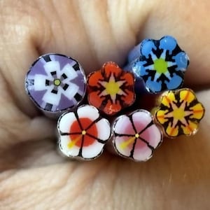 以下が含まれることがあります： 複雑な花柄が特徴の6本の円筒形ポリマークレイケーンのコレクション。紫、オレンジ、青、黄色、白、ピンクなどの様々な色があり、それぞれの端には独特の幾何学的な花の模様が施されています。