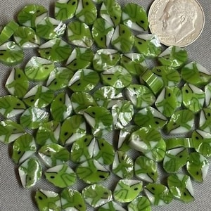 May include: A collection of small, flat, leaf-shaped glass beads featuring a marbled pattern of light green, dark green, and white. A silver-coloured United States dime is positioned in the upper right corner for scale, showing the size of the beads.
