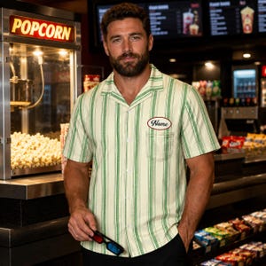 May include: A short-sleeve button-down shirt featuring vertical green stripes on a cream background. The shirt has a notched collar, a single chest pocket, and an oval-shaped patch on the left side with the word Name written in cursive script.
