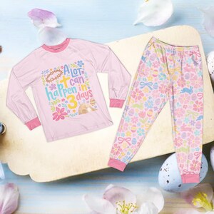 Op de afbeelding: Een lichtroze pyjamaset met een top met lange mouwen en een bijpassende broek. De top heeft de tekst "A lot can happen in 3 days" en illustraties met Pasen als thema. De broek is bedrukt met bloemen, konijntjes en paaseieren.