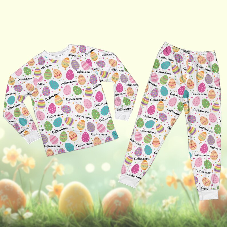 May include: Easter-themed pajama set in white, featuring a pattern of multi-coloured eggs. Each egg has a unique design and the words "Custom name". The set includes a long-sleeved top and matching trousers.
