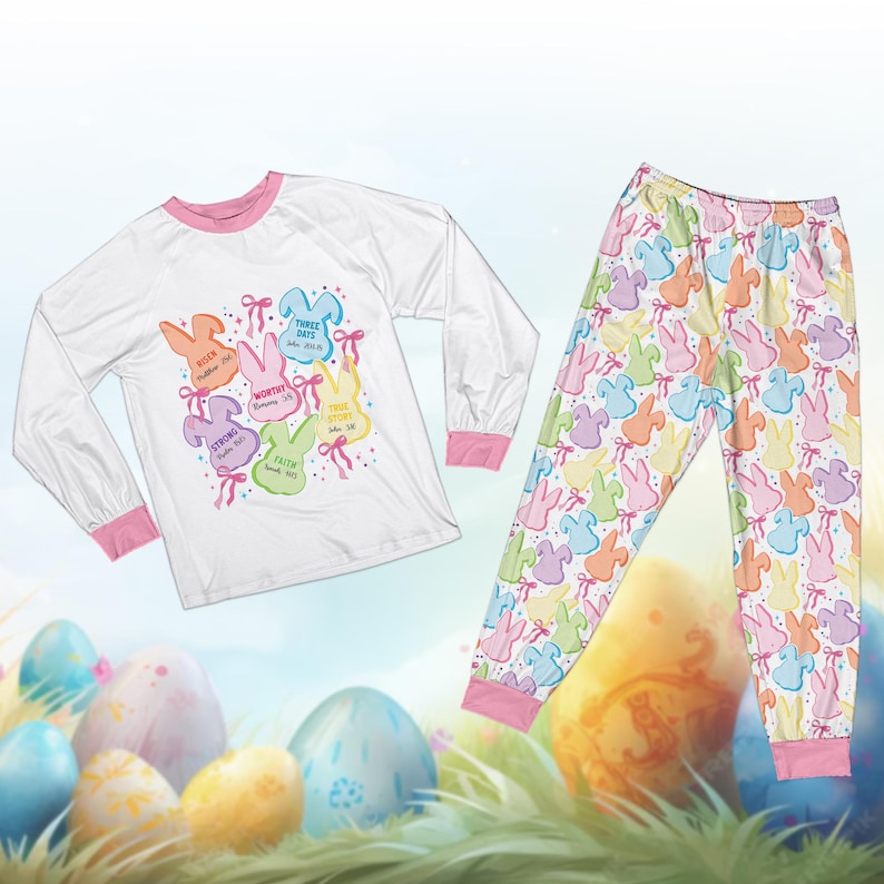 May include: White long-sleeve pajama top with pink trim and a colorful bunny graphic with text. Matching pajama pants feature a pastel bunny pattern. The Easter-themed sleepwear set is designed for comfort and style.