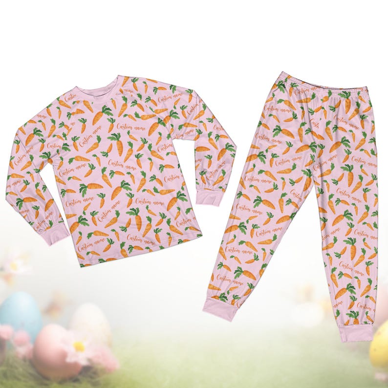 Pode incluir: Um conjunto de pijama rosa claro com um padr&atilde;o de cenoura. A parte superior de manga comprida e as cal&ccedil;as s&atilde;o cobertas por cenouras laranja com topos verdes e as palavras "Custom name" em letra cursiva. O pijama foi concebido para conforto e estilo.