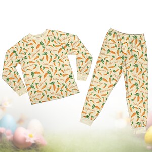 Pode incluir: Um conjunto de pijama de duas pe&ccedil;as com uma camisa de manga comprida e cal&ccedil;as. O conjunto &eacute; creme e coberto por um padr&atilde;o de cenouras laranja com folhas verdes e o texto "Custom name".