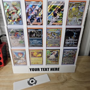 May include: White acrylic display stand with 10 slots for trading cards. The stand has a black label that says "YOUR TEXT HERE". The stand is filled with various Pokemon trading cards, including cards featuring Pikachu, Umbreon, Galvantula, and others.