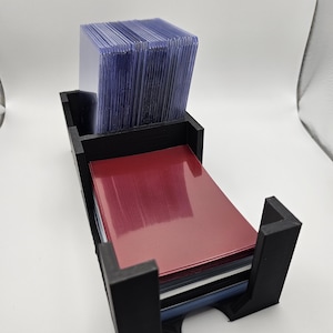 May include: A black plastic card holder with a clear plastic divider for storing cards. The holder is filled with a stack of red, blue, and white cards.