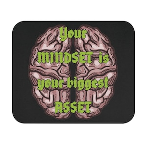 Może przedstawiać: Czarna podkładka pod mysz z ilustracją mózgu podzielonego na dwie połowy. Mózg jest różowy i brązowy z zielonym tekstem "Your mindset is your biggest asset."