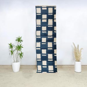 Moroccan wool runner rug featuring a cream square grid pattern on a deep navy blue background, handknotted by Berber artisans. This premium-quality wool rug offers a modern aesthetic with traditional craftsmanship, perfect for entryways, hallways, or kitchens. Its clean geometry, plush texture, and bold contrast make it ideal for contemporary, bohemian, or minimalist spaces seeking authentic Moroccan floor decor with structure and softness.