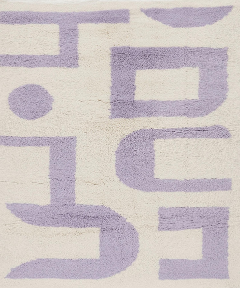 May include: A cream-colored rug with a repeating geometric pattern in lavender. The design features a series of connected shapes, including squares, rectangles, and a circle, creating a modern, abstract aesthetic. The rug has a soft, textured appearance.
