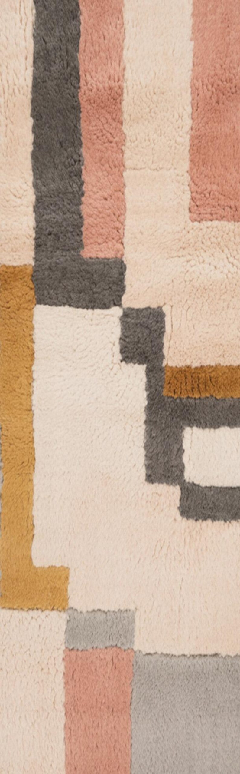 May include: A close-up of a textured rug with a geometric pattern. The rug features blocks of cream, gray, pink, and mustard yellow. The rug's design is modern and abstract, suitable for home decor.