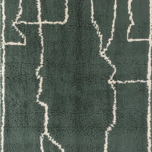 May include: A rectangular, dark green rug with a cream-colored, abstract geometric design. The design features a central shape with linear extensions and a cream-colored border. The rug has a textured, plush appearance.