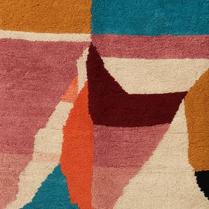 May include: Abstract geometric rug with a textured, plush surface. The rug features a patchwork design with blocks of color including teal, burgundy, orange, pink, cream, and gold. The rug's design is modern and colorful, suitable for a living room or bedroom.