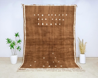 May include: A large, rectangular brown rug with a cream-colored border and white dot pattern. The rug has a shaggy texture and a fringe along the bottom edge. The rug is displayed against a white background.