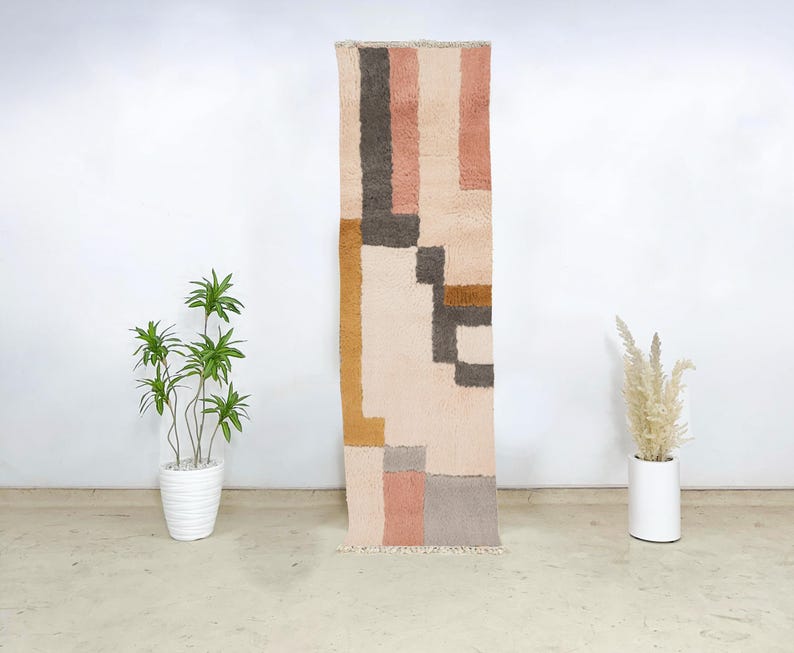 This hand-knotted Moroccan Beni Ourain runner rug showcases a harmonious geometric pattern in blush, mustard, grey, and cream wool. Woven by Berber women using traditional techniques, it features soft, color-blocked sections that bring warmth and structure to boho or modern interiors. The artisan-crafted texture and soothing palette make this wool runner ideal for entryways, hallways, or narrow spaces looking for both coziness and design impact.